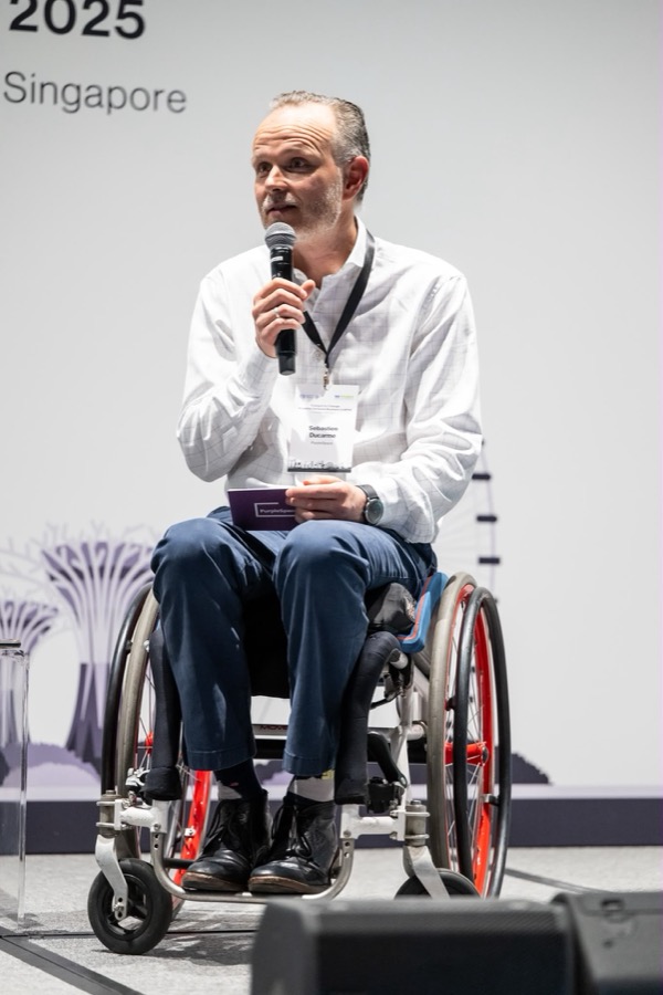 Seb speaking into a microphone on stage at a disability inclusion conference in Singapore